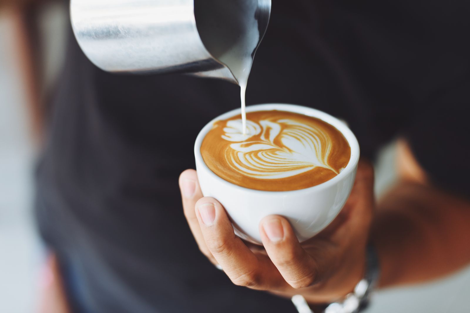 A white cup of coffee while milk is poured in.