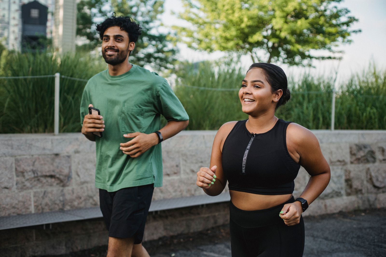 Two people jogging side by side on a city path and smiling.
